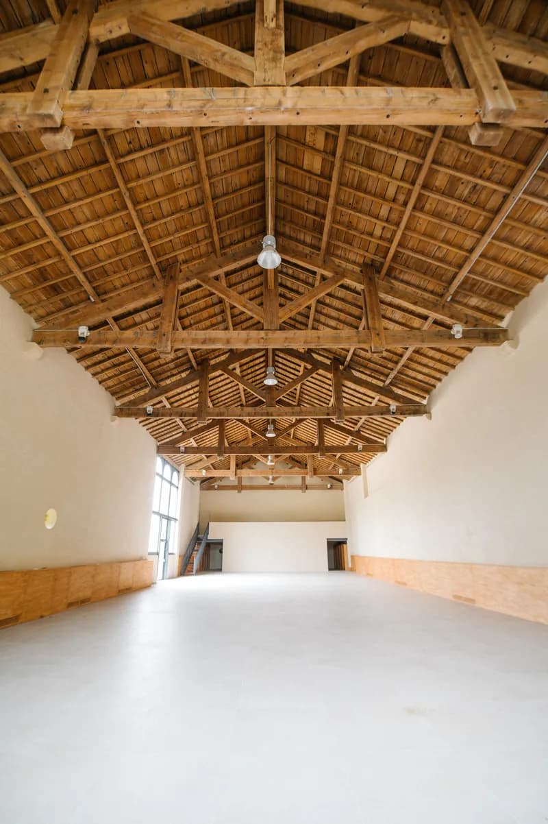 Large empty reception hall under a timber roof, lit by a glazed bay