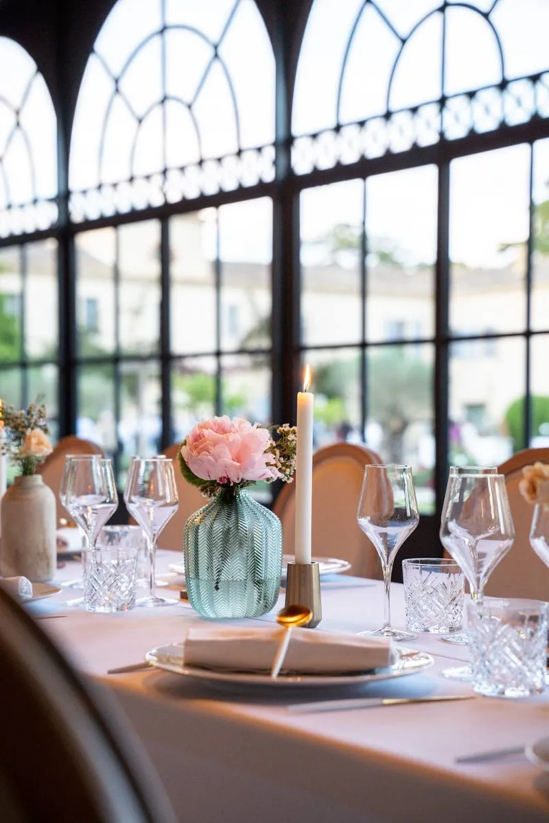 Table set in front of arched glass windows, with a pink peony and a candle