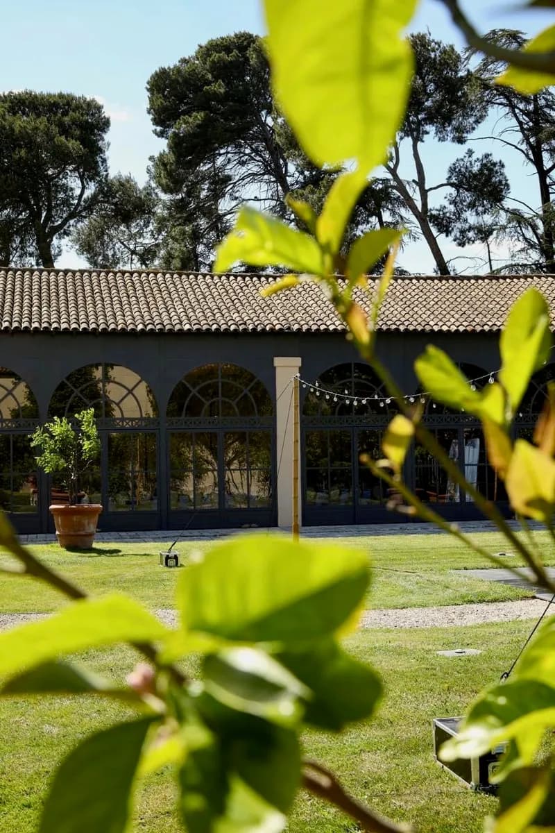 Building with arched glass windows seen from the lawn, beneath pine trees