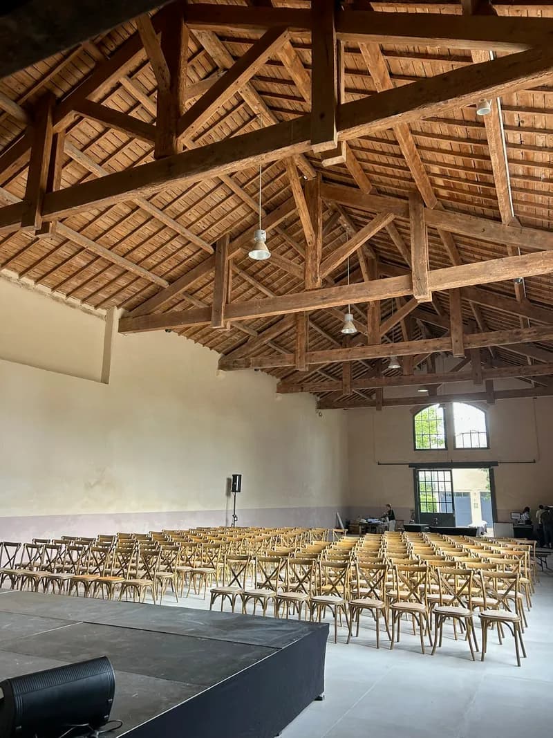 Hall laid out in rows of chairs facing a stage, beneath the timber roof
