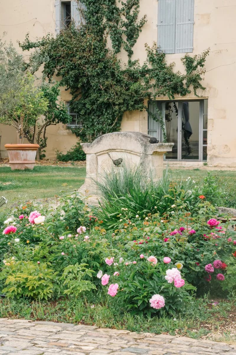 Stone well surrounded by a bed of peonies and roses in front of the façade