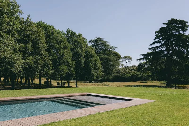 Swimming pool edged with a wooden deck, surrounded by lawn and trees