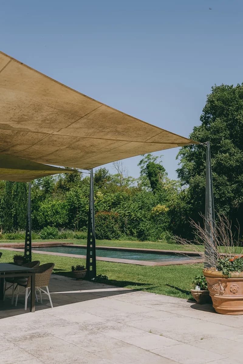 Terrace shaded by a stretched sail, with garden furniture facing the pool