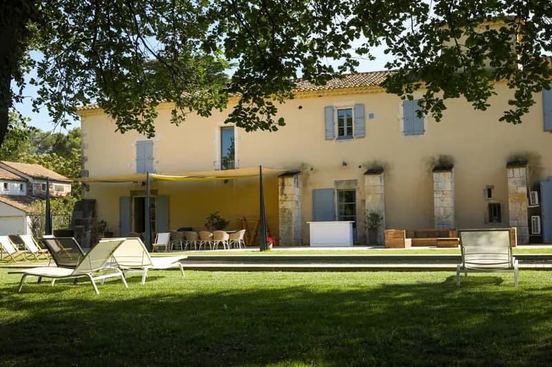 Sun loungers on the lawn before a building with blue shutters and a shaded terrace
