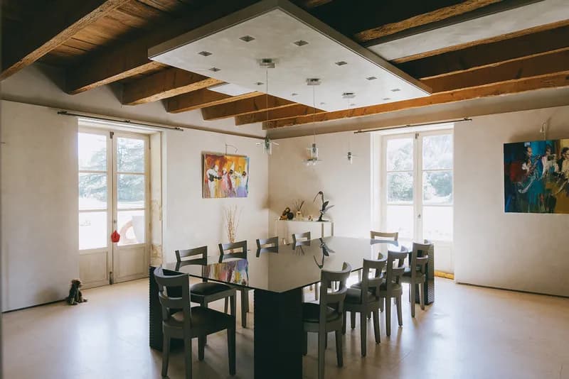 Dining room under exposed beams, with a large table and colourful paintings