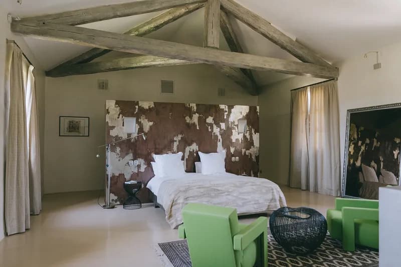 Bedroom under exposed roof beams, with a double bed and green armchairs