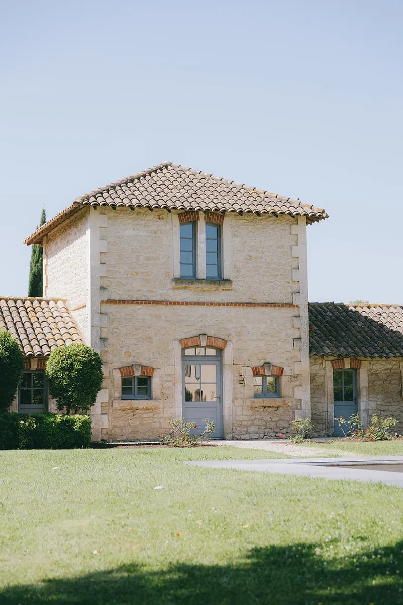 Stone building with blue shutters, surrounded by lawn and rose bushes